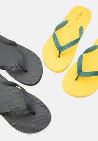 Deux paires de tongs, une jaune avec des brides vertes et une grise avec des brides assorties, disposées sur un fond blanc.