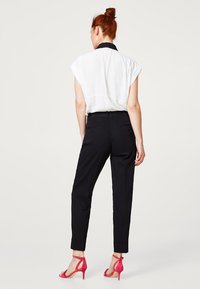 Bílá krátká halenka s černým límečkem, doplněná černými úzkými kalhotami a růžovými sandály na vysokém podpatku. Minimalistický design.
