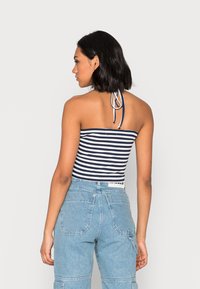 Top de tubo listrado em azul-marinho e branco com atilhos de pescoço halter, combinado com calças de ganga de cintura alta em azul claro, com grandes bolsos.