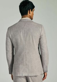 Hellegraue Leinenjacke mit tailliertem Schnitt, eingeprägtem Revers und einem einzelnen Schlitz. Besitzt einen strukturierten Stoff und Knopf-Details an den Ärmeln.