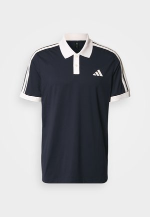 Marineblå poloshirt med hvid krave og ærmekanter. Har tre hvide striber på hver skulder og et lille logo på brystet.