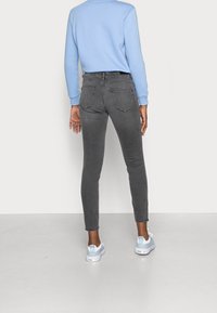 Vaqueros ajustados grises de tiro medio, con bolsillos traseros y detalles de costura sutiles, combinados con una sudadera azul claro y zapatillas.