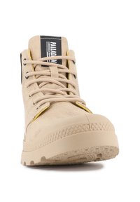 Botas altas beige con superiores de lona texturizada. Detalles amarillos a lo largo de los ojetes, cordones planos y suelas de goma con un dibujo en relieve.