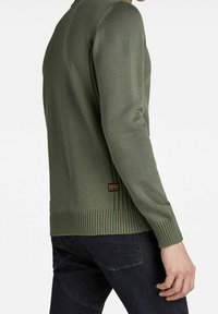 Grüner Strickpullover mit langen Ärmeln, gerippten Bündchen und Saum, mit einem kleinen Markenlabel hinten in der Nähe der Taille.