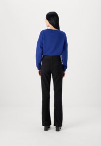Blå oversized hettegenser med lange ermer, kombinert med svarte vide bukser. antrekket har et glatt stoff og minimalistisk design.