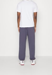 Miestenská súprava pozostávajúca z jednoduchého bieleho trička s krátkym rukávom a voľných tmavošedých teplákov. Športové topánky s bielymi a červenými detailmi.