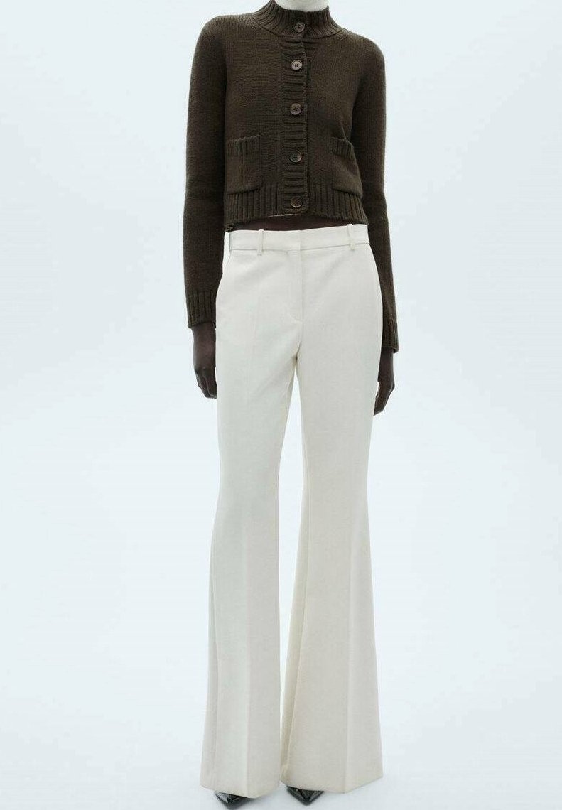 Cardigan boutonné marron foncé avec poches sur le devant, associé à un pantalon blanc taille haute à jambes larges et des chaussures noires pointues.