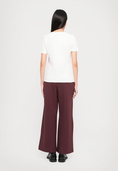 Weißes T-Shirt mit kurzen Ärmeln, kombiniert mit burgunderfarbenen, weit geschnittenen Hosen, mit glatter Textur und minimalistischem Design. Schwarze Schuhe runden den Look ab.