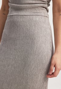 Siva teksturirana krila, izdelana iz elastičnega materiala z vertikalnim rebrastim vzorcem. Podrobni posnetek prikazuje gladek pas in suh silhuet.