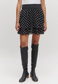 Zwarte rok met stippenpatroon en gelaagd ontwerp, met smocktaille, gemaakt van lichte stof. Gecombineerd met zwarte laarzen tot de knie met hak.