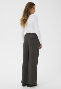 Hoge taille, wijde broek in donkergrijs met streepjes; heeft een achterzak en een gladde stof. Gecombineerd met een witte top met lange mouwen.