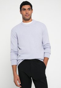 Pulover tricotat mov deschis, cu guler rotund și manșete ribbed, asortat cu pantaloni negri. Are un material texturat.