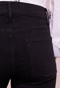Jeans de mezclilla negra con cintura alta, que cuentan con dos bolsillos traseros y sutiles detalles de costura. Textura suave y forma ajustada.