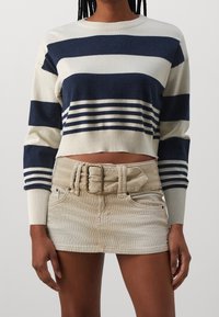 Pull rayé bleu marine et crème avec des poignets côtelés, assorti à une mini-jupe en velours côtelé beige avec une ceinture épaisse décorative.