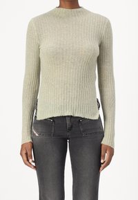 Pull vert clair côtelé avec un col montant, des manches longues et un ourlet brut. Porté avec un jean gris foncé ajusté avec des poches zippées.