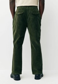 Dark green corduroy pants with a straight cut, featuring two back pockets and black chunky boots. Textured fabric with vertical stripes.