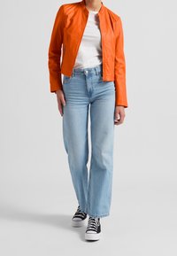 Giacca bomber in pelle arancione, t-shirt bianca a girocollo, jeans a gamba dritta azzurri chiari e sneakers nere con suole bianche.