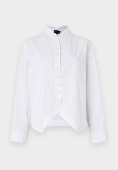 Balta pieguļoša krekls ar stāvošu apkakli, pogu priekšu, garām piedurknēm un noapaļotu apakšmalu, izgatavots no gludas kokvilnas maisījuma auduma.