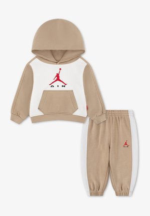 Béžová a biela tepláková súprava pre batoľatá s mikinou s kapucňou a nohavicami, červené logo Jumpman Air na hrudi a ľavej nohe, klokanie vrecko na mikine.