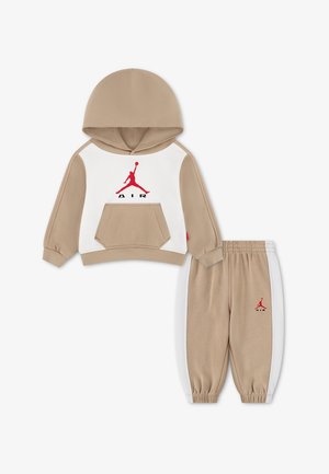 Beżowo-biały dres dziecięcy z kapturem i spodniami, czerwone logo Jumpman Air na klatce piersiowej i lewej nogawce, kieszeń kangurka na bluzie.