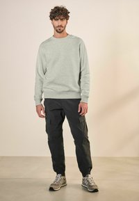 Helles graues Sweatshirt mit Rundhalsausschnitt, kombiniert mit schwarzen Cargo-Hosen mit Seitentaschen. Das Modell trägt beigefarbene Sneakers mit grauen Akzenten.