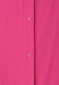 Tissu rose avec deux boutons translucides cousus au centre, montrant la patte de boutonnage verticale et les détails des coutures.