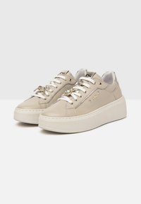 Zapatillas de cuero beige con un acabado suave, suela gruesa blanca, elementos decorativos dorados y cierre con cordones. Diseño de punta redonda.