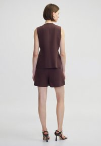 Bruine mouwloze top gecombineerd met bijpassende shorts. De stof heeft een gestructureerde textuur. De outfit wordt aangevuld met sandalen met hoge hakken en bandjes.