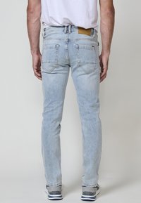 Svetlo modré denimové džínsy so slim fit strihom, obsahujúce dve zadné vrecká, viditeľné švy a hnedú koženú nášivku na páse.