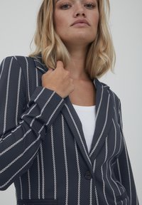 Mornarsko prugasta jakna s bijelim vertikalnim prugama, s jednom dugmadi, izrezom u obliku vrha i elegantnim, krojenim dizajnom.