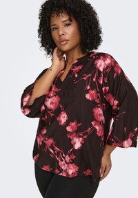 Black blouse with pink floral pattern, relaxed fit, V-neckline, three-quarter sleeves, textured fabric, and side slits at the hem.