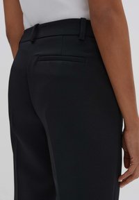 Pantaloni neri su misura con una texture liscia, dotati di una tasca posteriore piatta e passanti per cintura. Design semplice e strutturato con una vestibilità dritta.