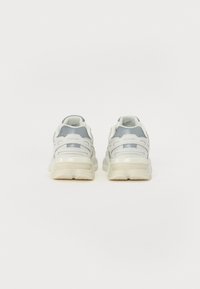Zapatillas blancas con acentos grises, hechas de material sintético, con una suela gruesa, paneles de malla y un logotipo grabado en el talón.