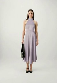 Rochie fără mâneci, de culoare lavandă, cu un guler înalt, talie strânsă și fustă evazată. Modelul ține în mână o geantă de umăr neagră și poartă pantofi cu toc negri.