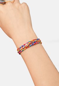 Bracelet tressé coloré avec des cordons rouges, bleus, jaunes et oranges, rehaussé de détails métalliques ronds ornés de petites pierres précieuses.