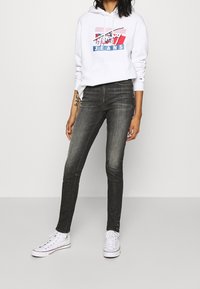 Biała bluza z kapturem z wielokolorową grafiką i tekstem, w połączeniu z szarymi dżinsami slim-fit i białymi trampkami. Casualowy strój o prostym stylu.