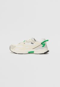Sneaker con una toma superiore in rete di color crema e grigio chiaro, dettagli verdi, suola in gomma nera e cuciture a contrasto. Presenta una chiusura con lacci.
