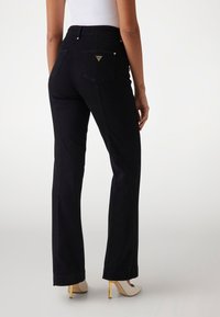 Pantalones negros de talle alto con pierna recta, que presentan detalles en dorado y bolsillos traseros con un logotipo en forma de triángulo.