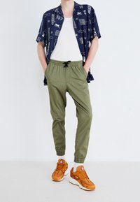 Kortärmad marinblå skjorta med vita tryck, kombinerad med olivgröna elastiska byxor och orange sneakers med vita sulor och detaljer.