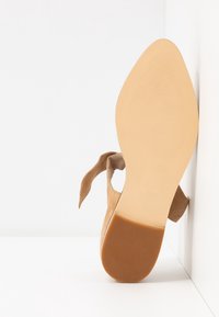 Chaussure à talons en daim beige avec un bout pointu et une sangle nouée à la cheville. Semelle extérieure lisse beige avec une texture rayée. Taille 37 visible.