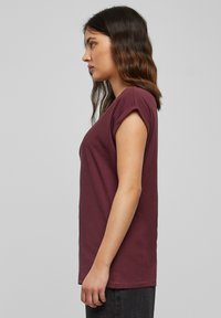 T-shirt bordeaux con maniche corte arrotolate, realizzato in cotone morbido, con colletto rotondo semplice e orlo dritto.