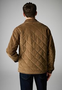 Pruun corduroy vooderdatud jakk, millel on teemantmuster, krae ja pikad varrukad. Nähtavad õmbluse detailid ja lõdvestatud lõige.
