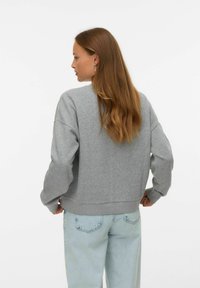 Felpa grigia con un fit rilassato, maniche lunghe, bordi a costine e texture morbida. Abbinata a jeans azzurri, vista da dietro.