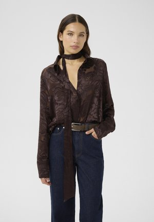 Chemise à manches longues, marron foncé avec un motif floral. Elle possède un col, un détail de cravate et est associée à un pantalon en denim taille haute.