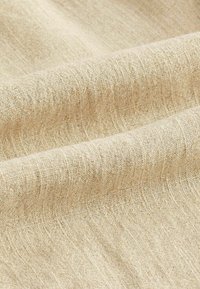 Beige gewebter Stoff mit einer strukturierten Oberfläche, die ein dezentes horizontales Muster und ein sanftes, natürliches Aussehen zeigt.