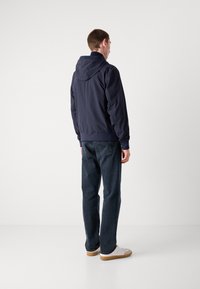 Marineblauwe hoodie met elastische manchetten en zoom, gecombineerd met donkere denim jeans en witte sneakers. Glad, lichtgewicht materiaal met minimale details.
