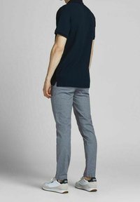 Granatowa prążkowana koszulka polo z krótkim rękawem, zestawiona z jasnoszarymi spodniami i białymi trampkami, ukazująca dopasowaną sylwetkę od tyłu.