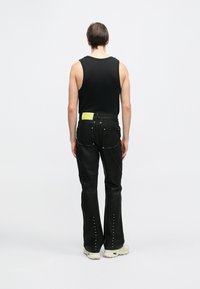 Crna bezrukavna majica i crne hlače s žutim detaljima, s ravnim nogavicama i zakovicama duž bočnih strana.