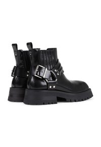 Botas de tobillo de cuero negro con un panel texturizado negro, detalle de hebilla plateada, suela de goma gruesa y lengüetas en la parte trasera para facilitar su puesta.