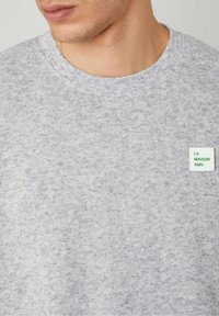 Felpa grigia realizzata in tessuto morbido, con un motivo testurizzato. Presenta un collo a giro e un piccolo etichetta verde e bianca cucita.